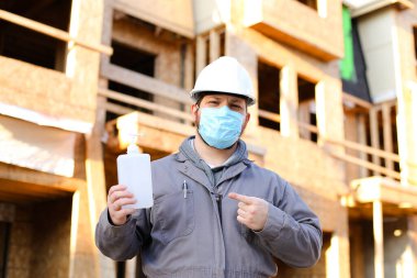 Foreman maske takıyor ve dezenfektan gösteriyor..