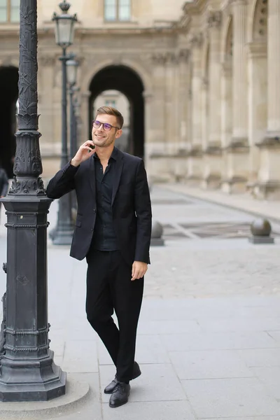 Joven hombre caucásico caminando en París y usando traje negro . — Foto de Stock