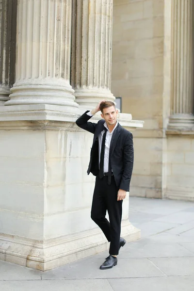 Junger Mann in schwarzem Anzug und Krawatte lehnt an Baukolonne. — Stockfoto