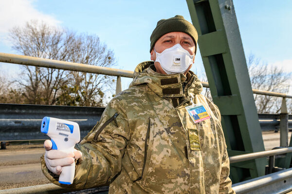 Chop, Ukraine - February 25, 2020: A border guard holds a digital thermometer during temperature control of citizens crossing the border at Ukrainian checkpoints. Coronavirus protection in Ukraine.