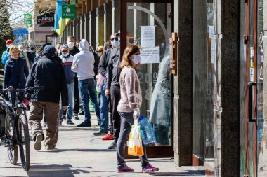 Uzhgorod, Ukrayna - 11 Nisan 2020: Koronavirüs nedeniyle karantina sırasında tıbbi maskeli insanlar dükkanın önünde yemek kuyruğunda bekliyorlar.