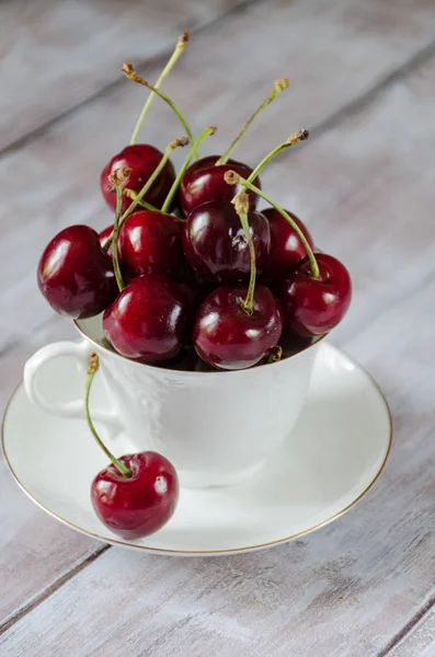 Cherry in a white cup on a light wooden background vertically — Stock Photo, Image