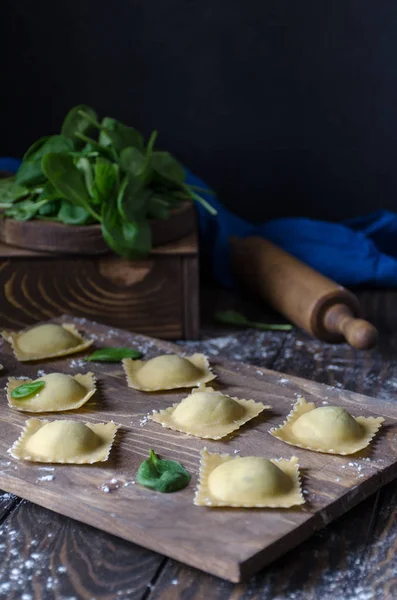 Not cooked ravioli on a wooden board, in the background a rolling pin and spinach — Stock Photo, Image