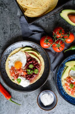 Huevos Rancheros Tostadas, Meksika kahvaltısı kızarmış tortilla, doğranmış domates ve soğan, jalapeno ve fasulye, üzeri kızarmış yumurta, avokado dilimleri ve ekşi krema ile servis edilir.