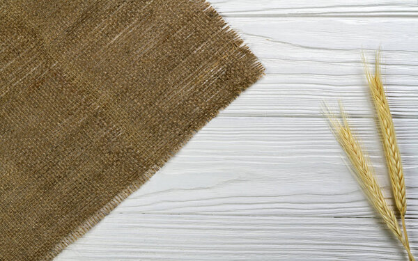 Wheat stalk and hessian fabric on white wooden background