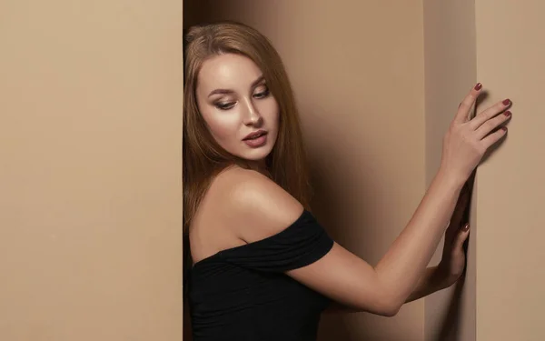 Jolie fille en robe noire appuyée sur le mur dans la chambre beige avec espace de copie — Photo