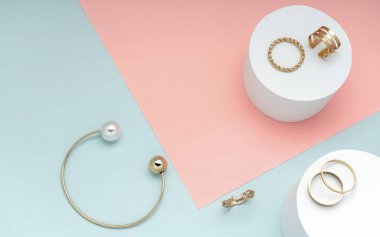 Düz altın ve inci bilezik ve altın yüzük koleksiyonu pembe ve yeşil kağıt arka planda.