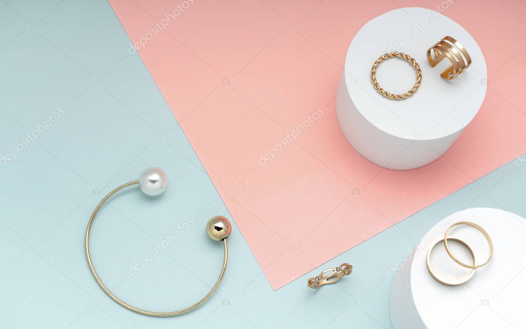 Flat lay of golden and pearl bracelet and golden rings collection on pink and green paper background
