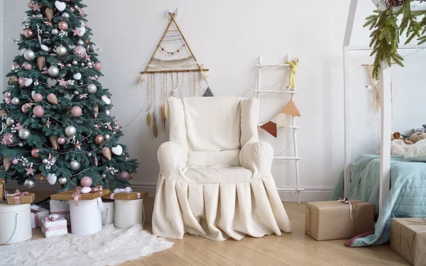 Duvarında bir merdiven ve düş kapanı asılı olan süslü Noel ağacının yanındaki klasik koltuk.