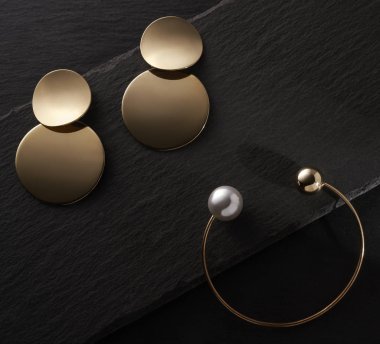 Altın küpeler ve siyah taş zemin üzerinde inci altın bilezikler.