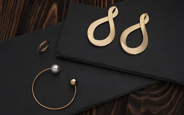 Золотой браслет, кольцо и бесконечность символа формы серьги пара на черной пластине — стоковое фото
