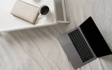 Kahve fincanının üst görüntüsü, yatağın üstünde kitap ve yatağın üstünde laptop.