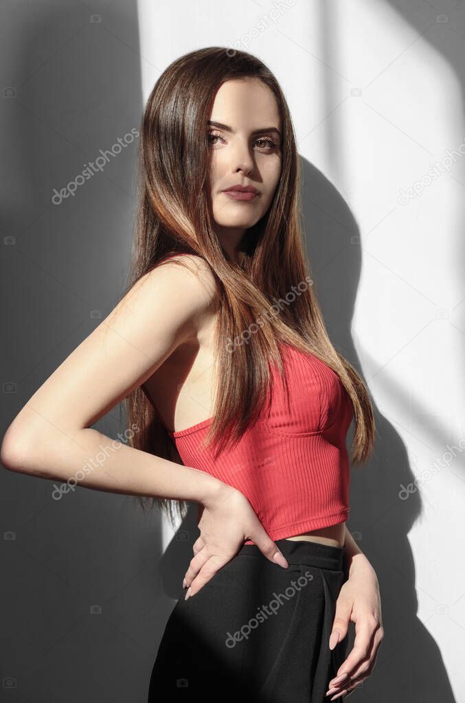 Beautiful girl wearing red crop top and posing while looking at the camera under sun light