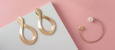 Sonsuzluk sembolü şekilli küpeler ve pembe ve beyaz kağıt arka planda incili modern bilezikler.