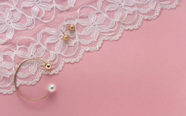 Oro con brazalete de perlas y pendientes dorados en textil blanco floral sobre fondo rosa con espacio para copiar — Foto de Stock