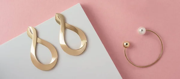 Бесконечность символа формы серьги и современный браслет с жемчугом на розовом и белом бумажном фоне — стоковое фото