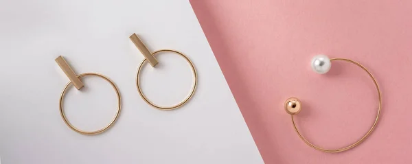 Foto panorámica de brazalete de oro y pendientes planas sobre papel rosa y blanco — Foto de Stock