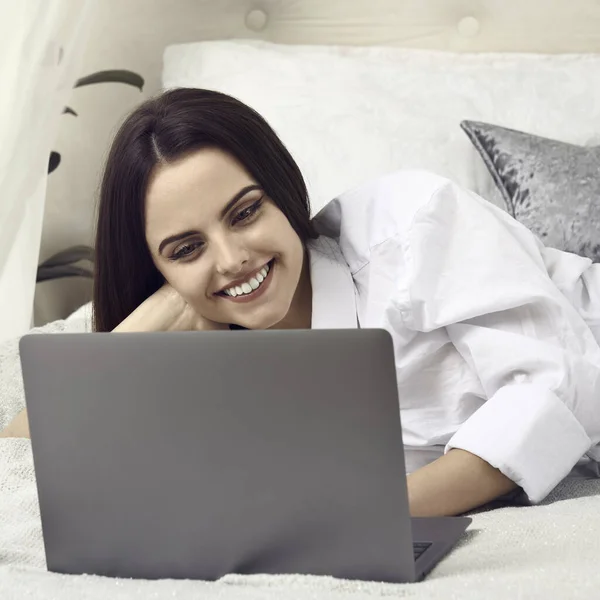 Szczęśliwa dziewczyna uśmiechnięta i korzystająca z laptopa w łóżku — Zdjęcie stockowe