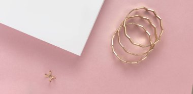 Altın modern bilezikler ve yüzük beyaz ve pembe arka planda kopya alanı ile