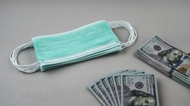Tıbbi koruma maskesi yığını ve para birikintileri gri arka planda