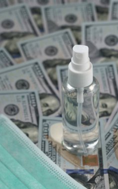 100 dolarlık banknotların ve maskenin üstüne alkol spreyi şişesi.
