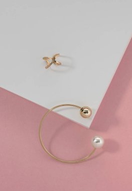 Pembe arka plan dikey beyaz kağıt üzerinde inci ve altın yüzüklü altın bileziğin üst görüntüsü