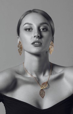 Dikey stüdyo çekimlerinde siyah elbiseli ve altın aksesuarlı çekici bir kız vardı.