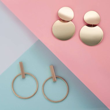 İki çift modern altın küpe pembe ve mavi geometrik desen üzerinde kağıttan yapılmış.