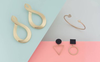 Modern tasarım mücevherlerinin soyut tasarımı. Pastel renkli kağıt arka planda altın küpeler ve bilezikler