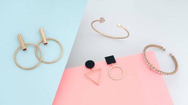 Mavi ve pembe kağıt arka planda modern altın bilezik ve küpeler