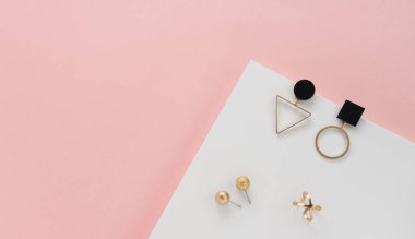 Geometrik tasarımın üst görüntüsü altın küpeler ve pembe ve beyaz zemin üzerinde yüzük