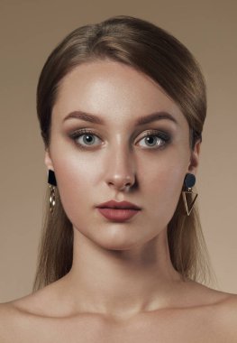 Bej arka planda geometrik tasarım küpeler takan güzel bir kızın dikey portresi