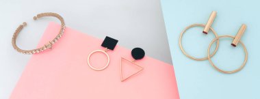 Modern altın mücevherler geometrik küpeler ve pembe ve mavi kağıtlar üzerinde bilezikler.
