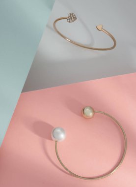 Pastel renk pembe ve mavi kağıt üzerinde zarif tasarım altın bilezikler dikey çekim