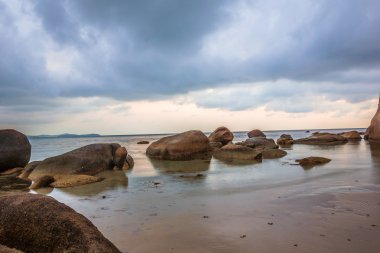 Büyük kayalar ile bir plaj yansıtan renkli kara bulutlar