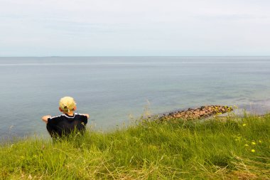 Bir yar, denizin yüksek te kenarında oturan çocuk