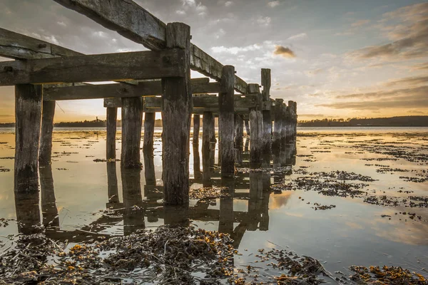 Viejo embarcadero de madera con postes reflejándose en el agua — Foto de Stock