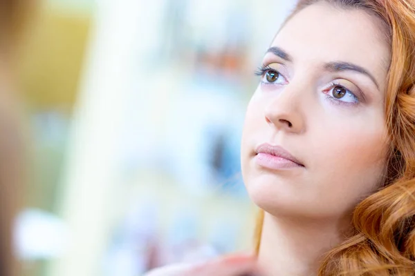 Red-haired girl with wavy hair in a beauty salon doing make-up. — Stock Photo, Image