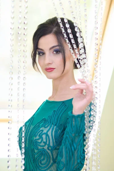 Modelo menina com cabelo escuro e um vestido turquesa posando depois de sua maquiagem feita e um novo penteado . — Fotografia de Stock