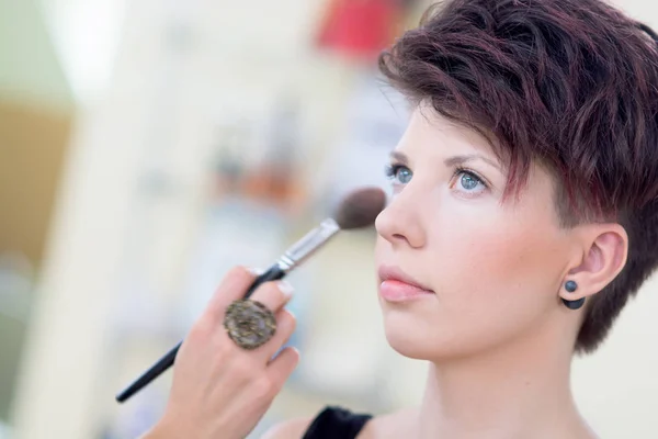 The girl with dark hair and short hair make make-up in a beauty salon. Shallow depth of field. — Stock Photo, Image