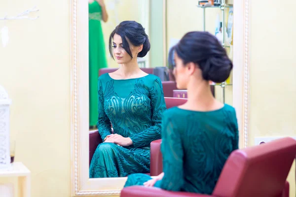 The girl with dark hair and a long dress sitting in the turquoise color barbers chair in front of the mirror after she did my hair. Focus on girl\'s reflection in the mirror.