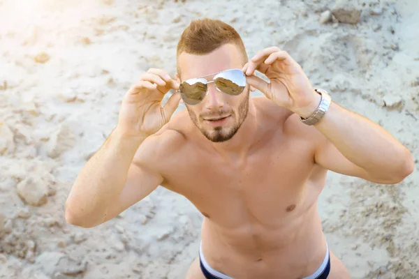 Uomo atletico in spiaggia guardando attraverso gli occhiali da sole . — Foto Stock
