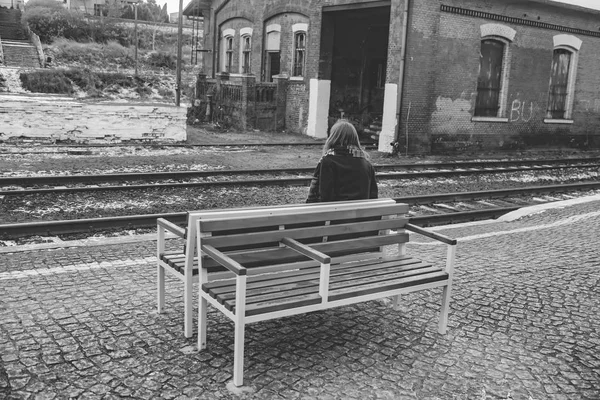 Egy lány ül egy padon a régi állomás peronján, várakozás-re a vasútállomástól. B w fotó — Stock Fotó