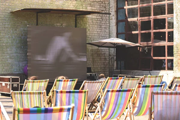 Summer cinema. People watch old movies sitting on beach chairs. Shallow depth of field.