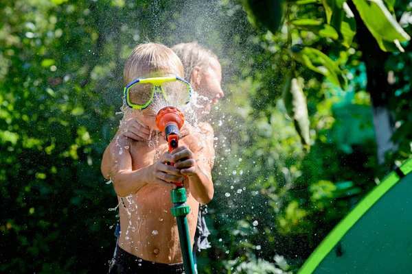 Joyful boy playing with water. The boy in hands holds a garden hose. Focus on boy