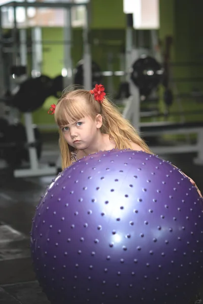 Malá dívka pózuje v tělocvičně v blízkosti velké gumový míček — Stock fotografie