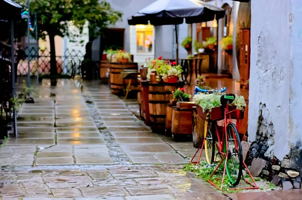 秋の雨の中で静かで居心地の良いさびれたストリートカフェ。花で飾られた古い自転車. — ストック写真