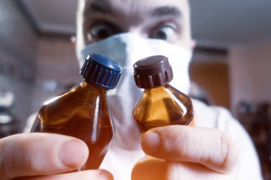 Elinde ilaç şişeleri olan bir adam. Yüzünde tıbbi bir maske var..