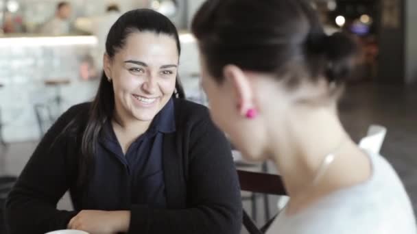 Dos mujeres jóvenes sentadas y hablando en la cafetería . — Vídeo de stock