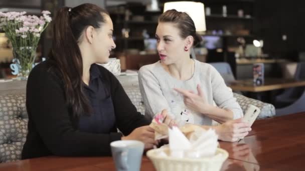 Dos mujeres jóvenes sentadas y hablando en la cafetería . — Vídeos de Stock